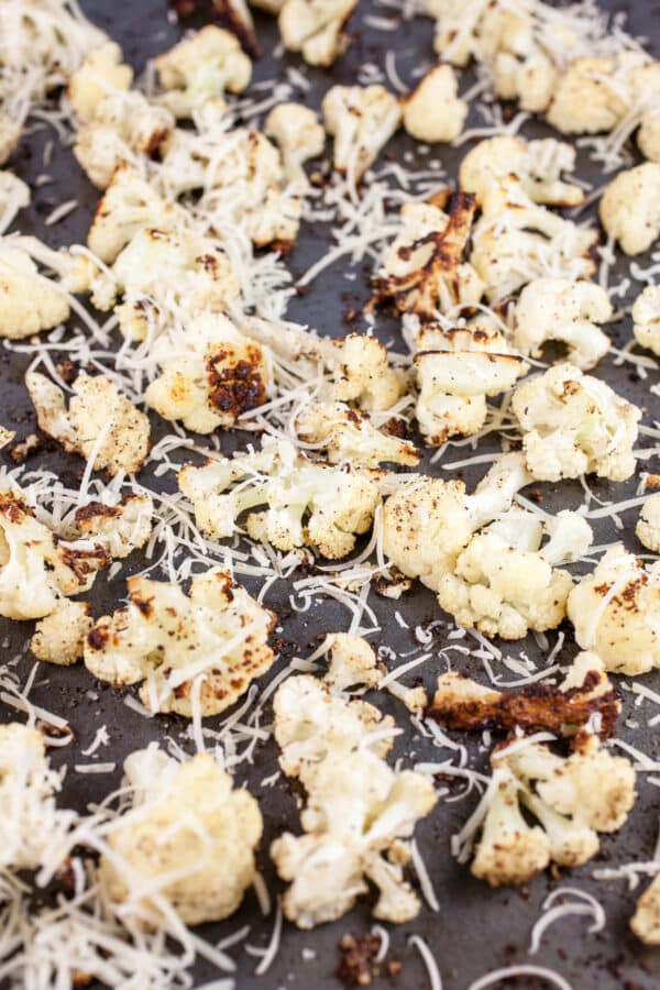 Roasted cauliflower with shredded Parmesan cheese on baking sheet.