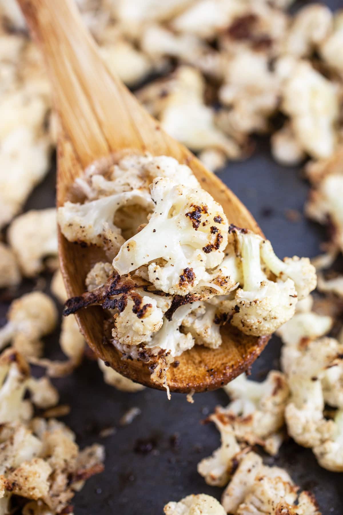 Roasted cauliflower on wooden spoon lifted from baking sheet.