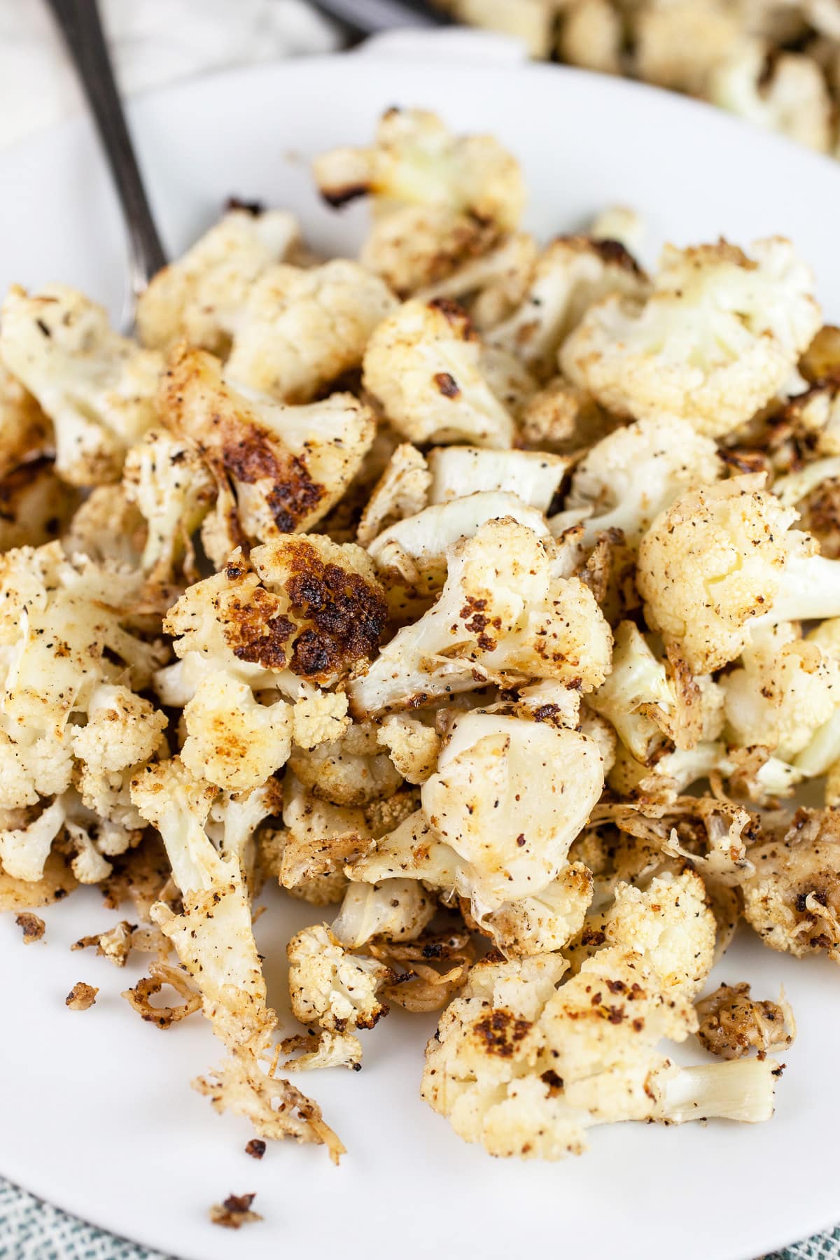 Roasted cauliflower with Parmesan cheese on white plate with fork.