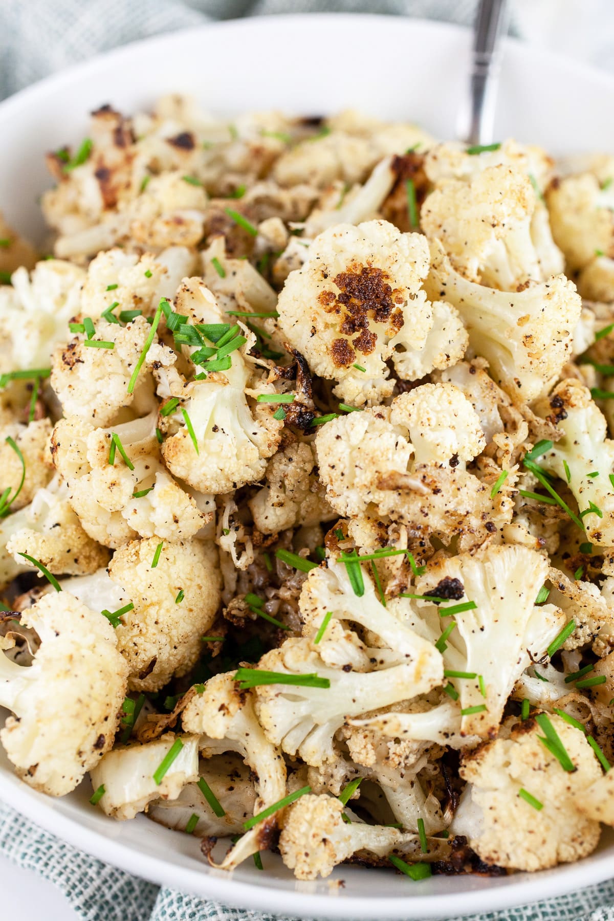 Garlic roasted cauliflower with minced chives in white bowl with spoon.