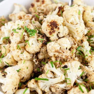 Parmesan roasted cauliflower with minced chives in white bowl.