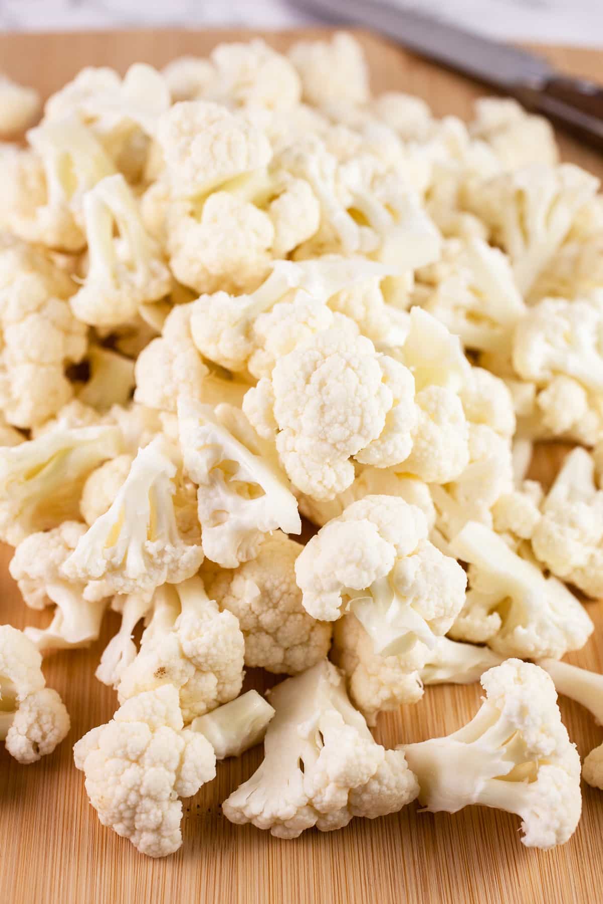 Cauliflower florets on wooden cutting board with knife.