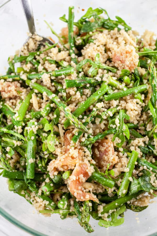 Smoked salmon arugula quinoa salad with asparagus combined in large glass mixing bowl.