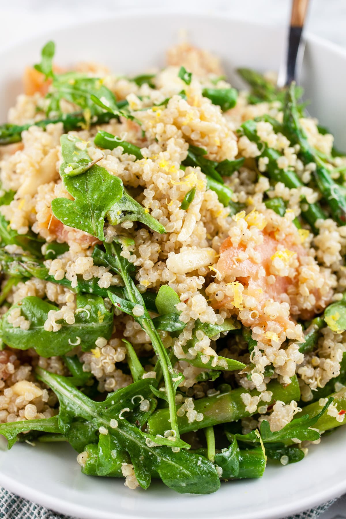 Smoked salmon arugula quinoa salad with asparagus in white bowl with fork.
