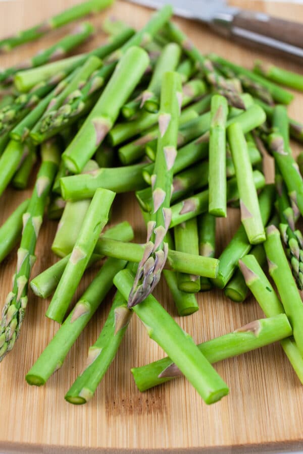 Raw chopped asparagus on wooden cutting board with knife.