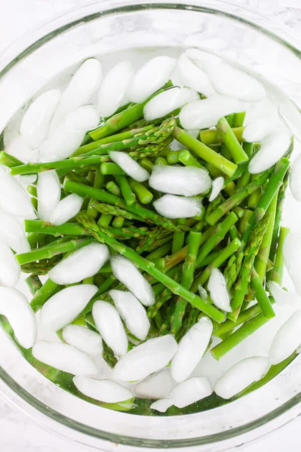 Blanched asparagus in bowl of ice water.