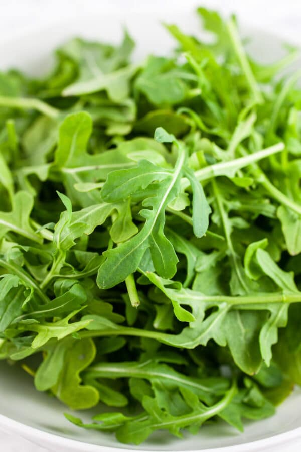 Raw arugula in white bowl.