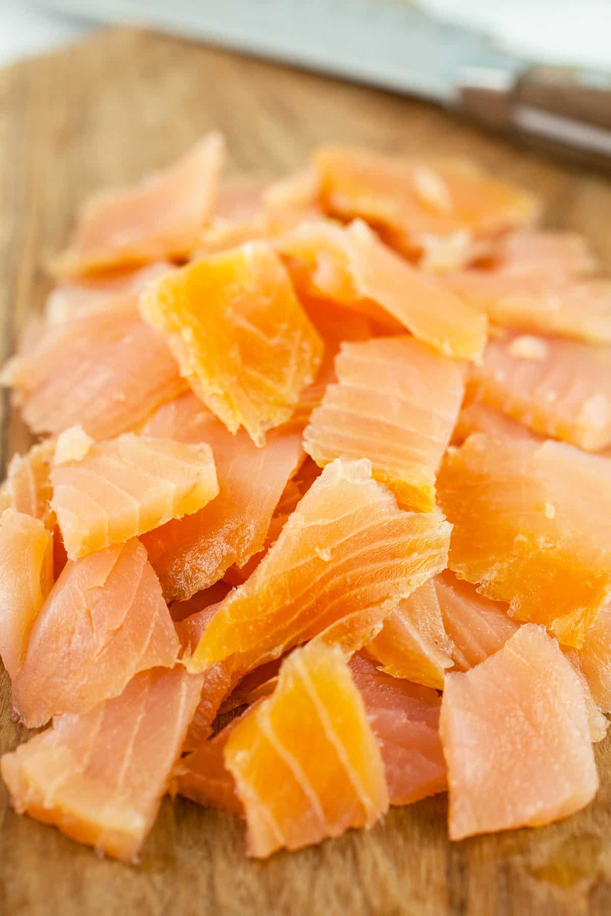 Chopped smoked salmon on wooden cutting board with knife.