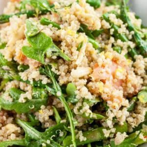 Smoked salmon arugula quinoa salad with asparagus in white bowl.