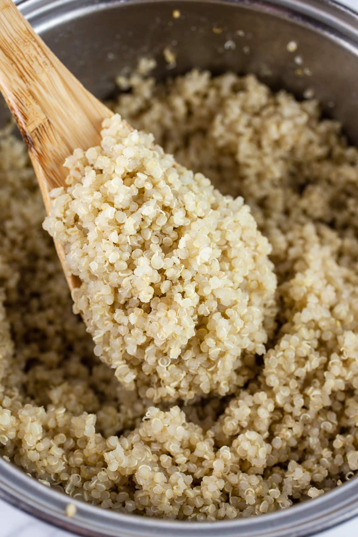 Cooked quinoa lifted with wooden spoon from sauce pan.