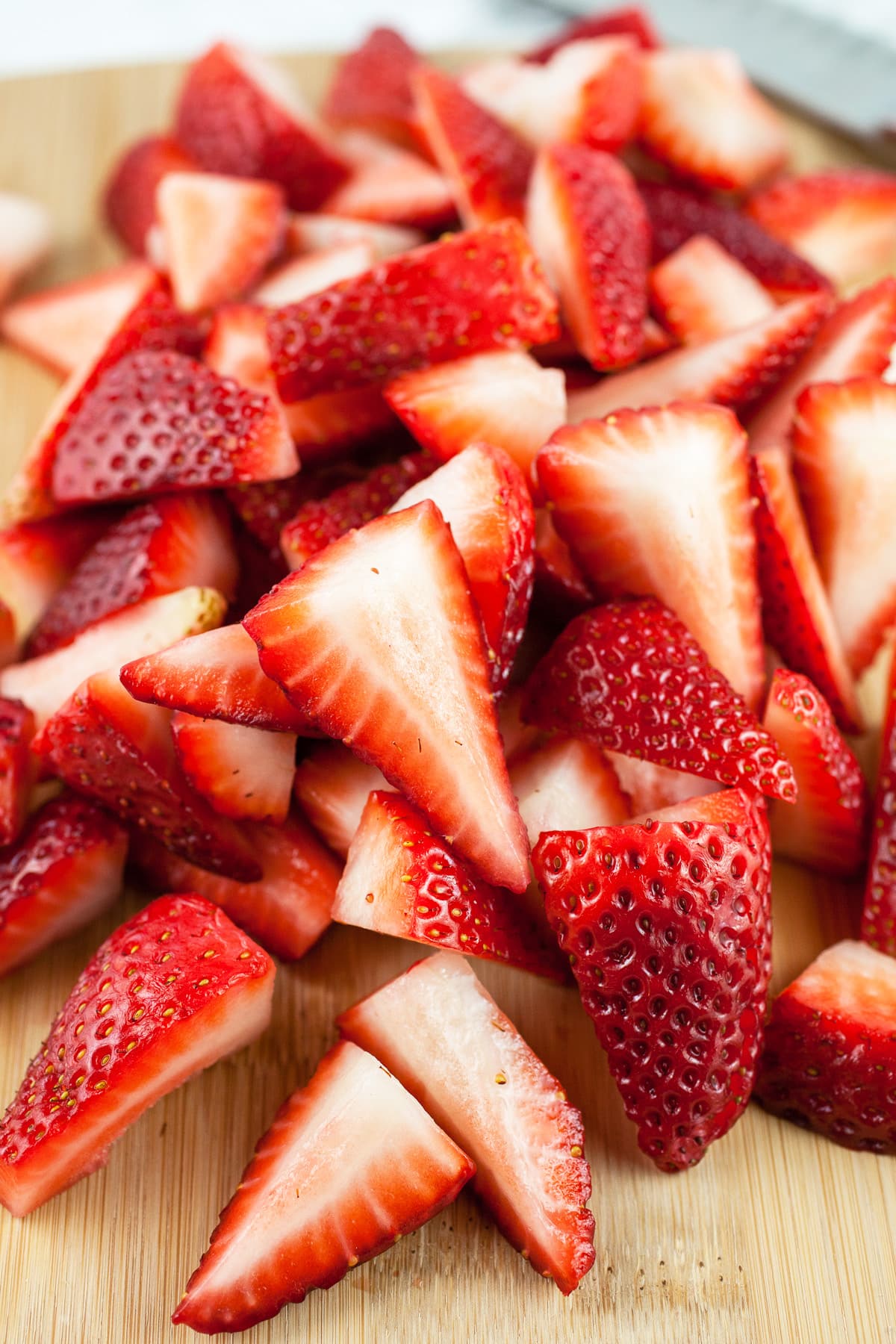 Fresh strawberries cut into chunks on wooden cutting board with knife.