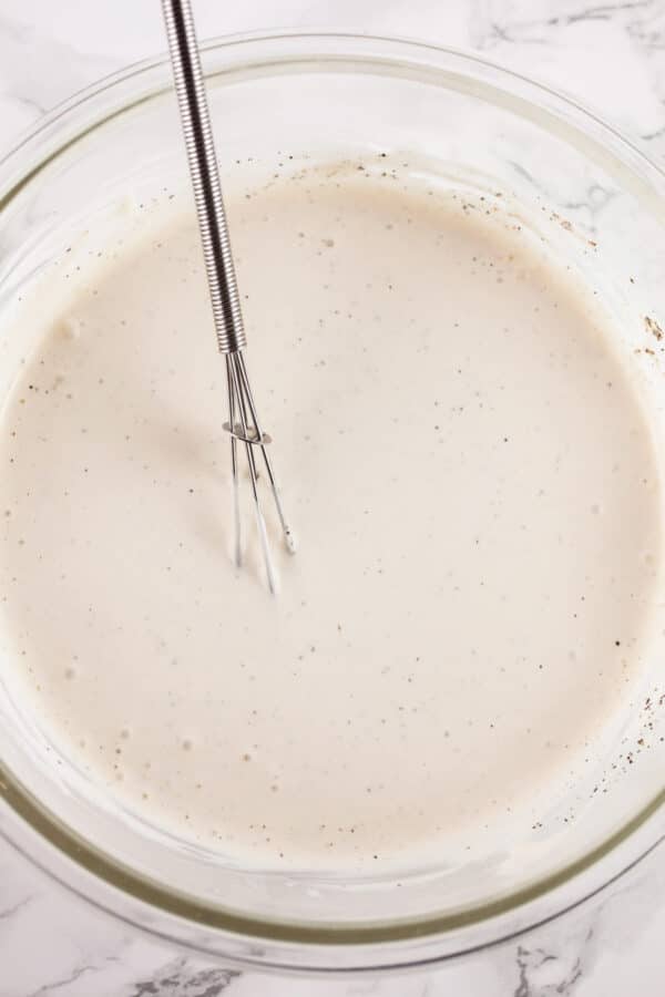 Creamy ingredients mixed together in glass bowl with whisk.