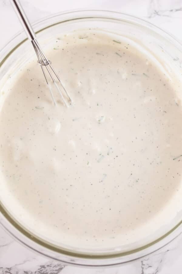 Creamy blue cheese dressing in glass bowl with small whisk.