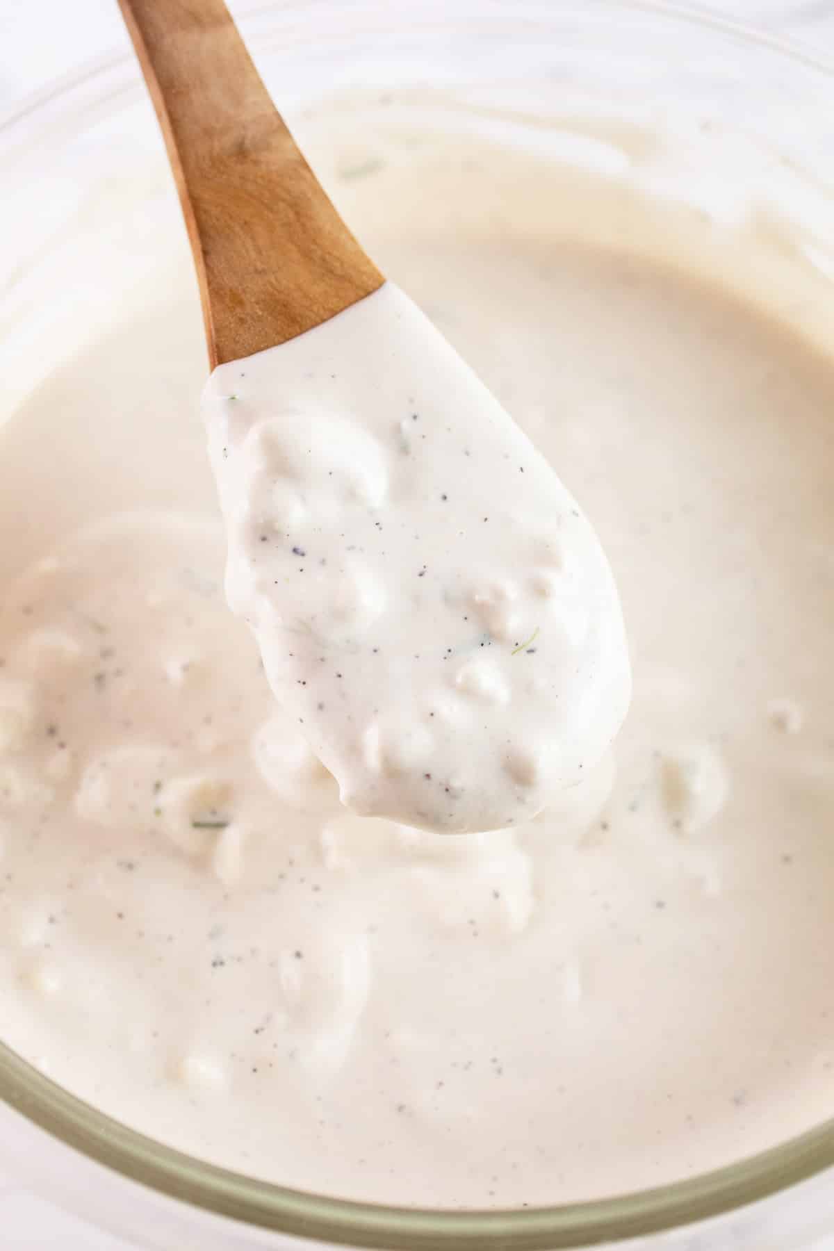 Blue cheese dressing with minced chives in glass bowl stirred with wooden spoon.