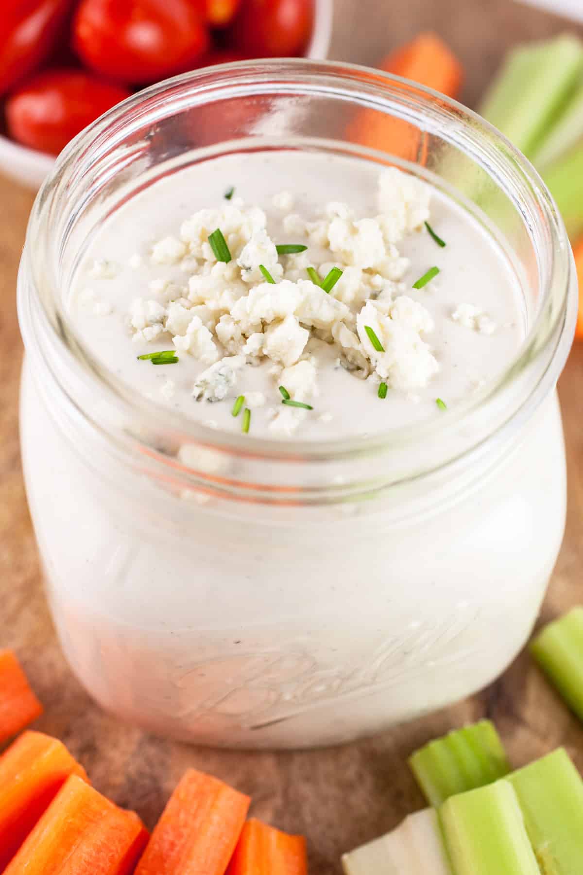 Chunky blue cheese dressing on wooden board with raw veggies.