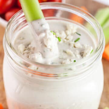 Celery stick dipped into jar of blue cheese dressing.