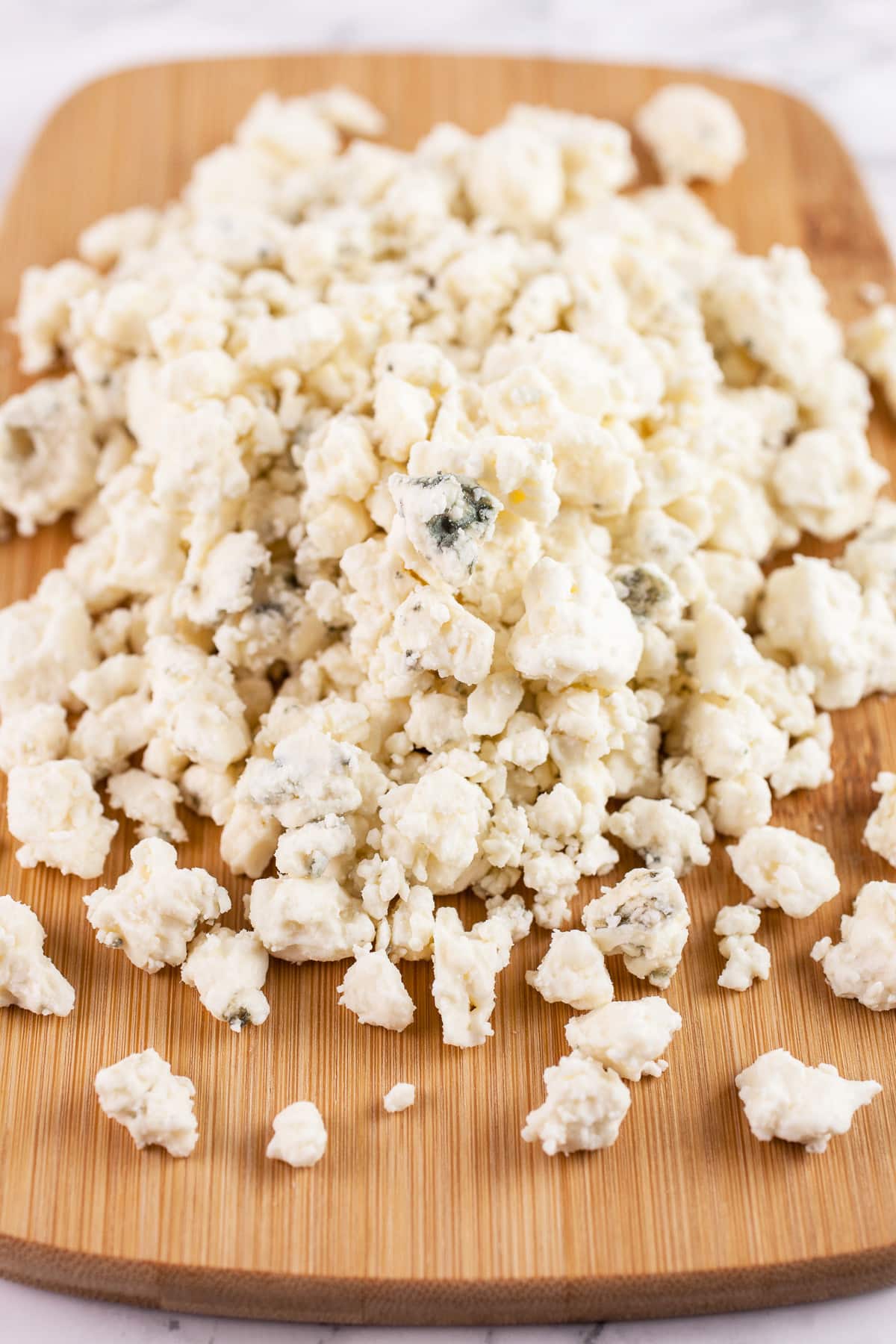 Blue cheese crumbles on wooden cutting board.