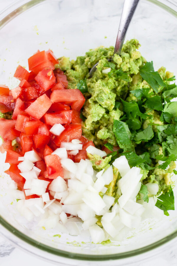 Diced onions, tomatoes, cilantro and avocado in glass bowl.