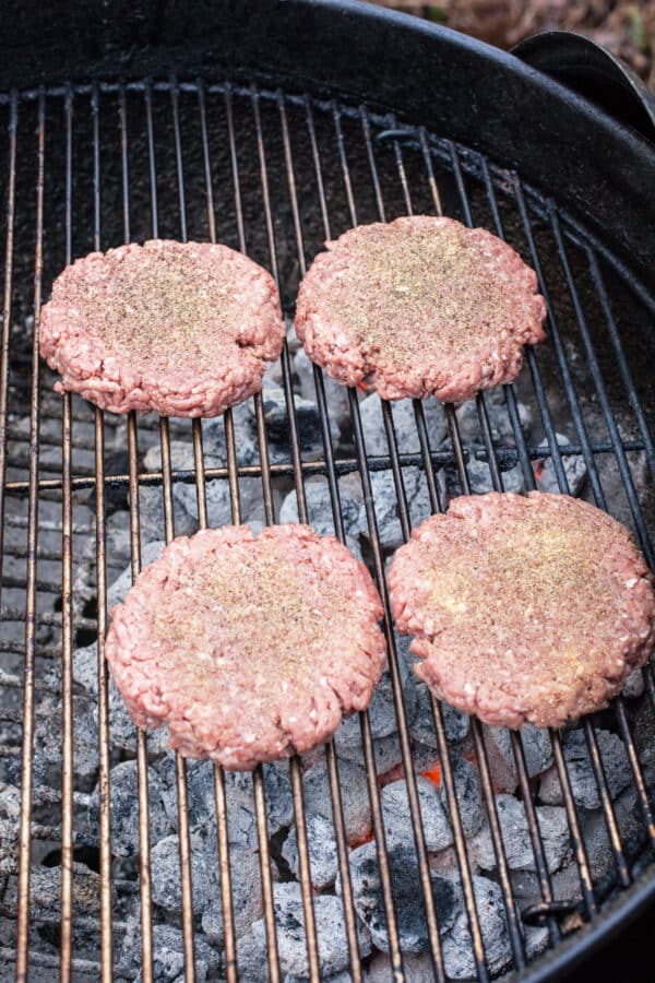 Uncooked ground beef patties on charcoal grill.