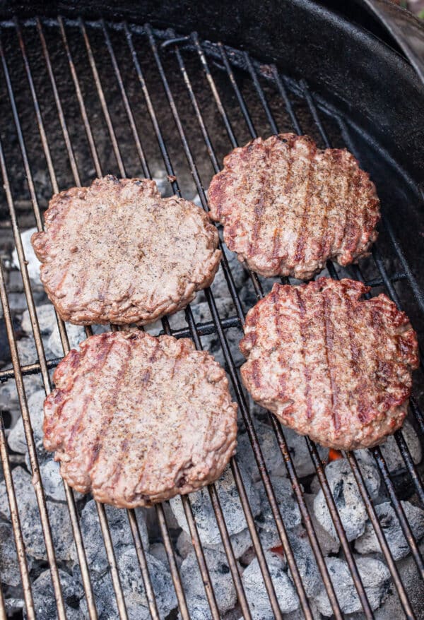 Cooked ground beef burger patties on charcoal grill.