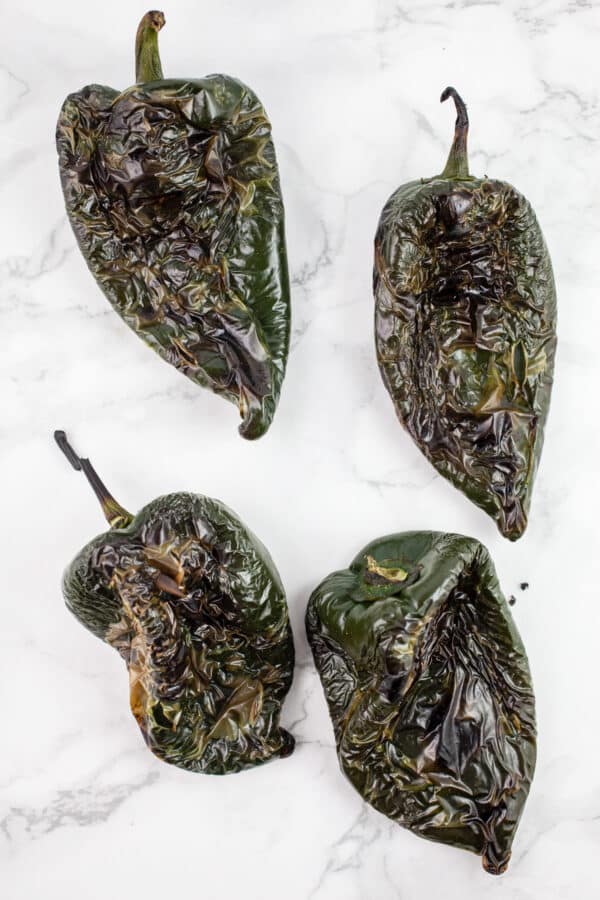 Whole roasted poblano peppers on white suface.