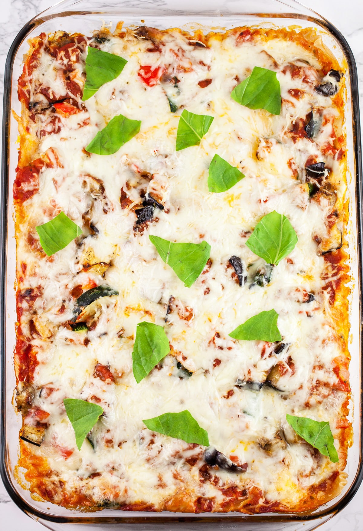 Garden vegetable lasagna with torn basil leaves in glass baking dish.