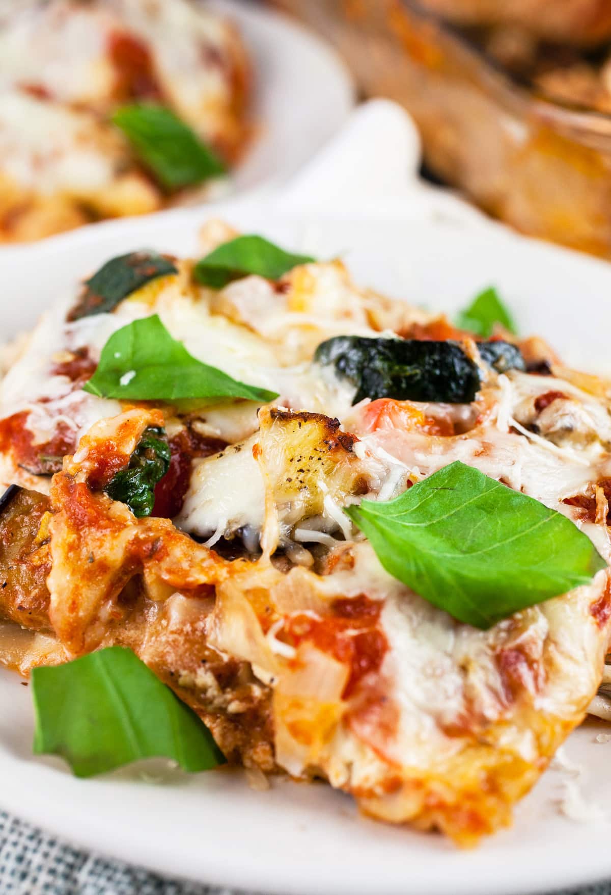Garden vegetable lasagna on white plate garnished with fresh basil leaves.