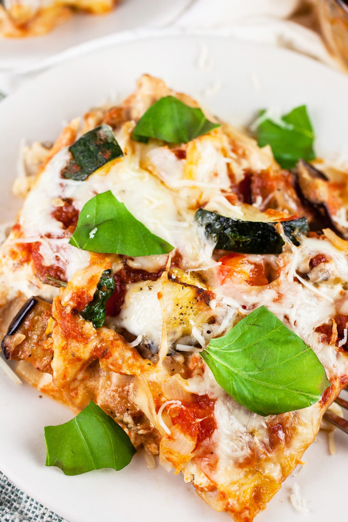Slice of garden vegetable lasagna on white plate garnished with fresh basil.