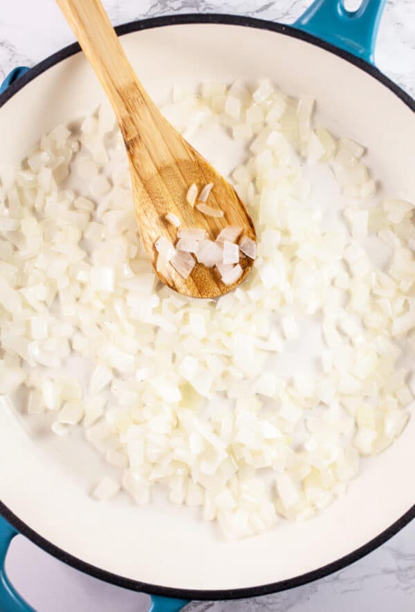 Minced garlic and onions sautéed in skillet with wooden spoon.