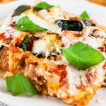 Slice of garden vegetable lasagna on white plate garnished with fresh basil.