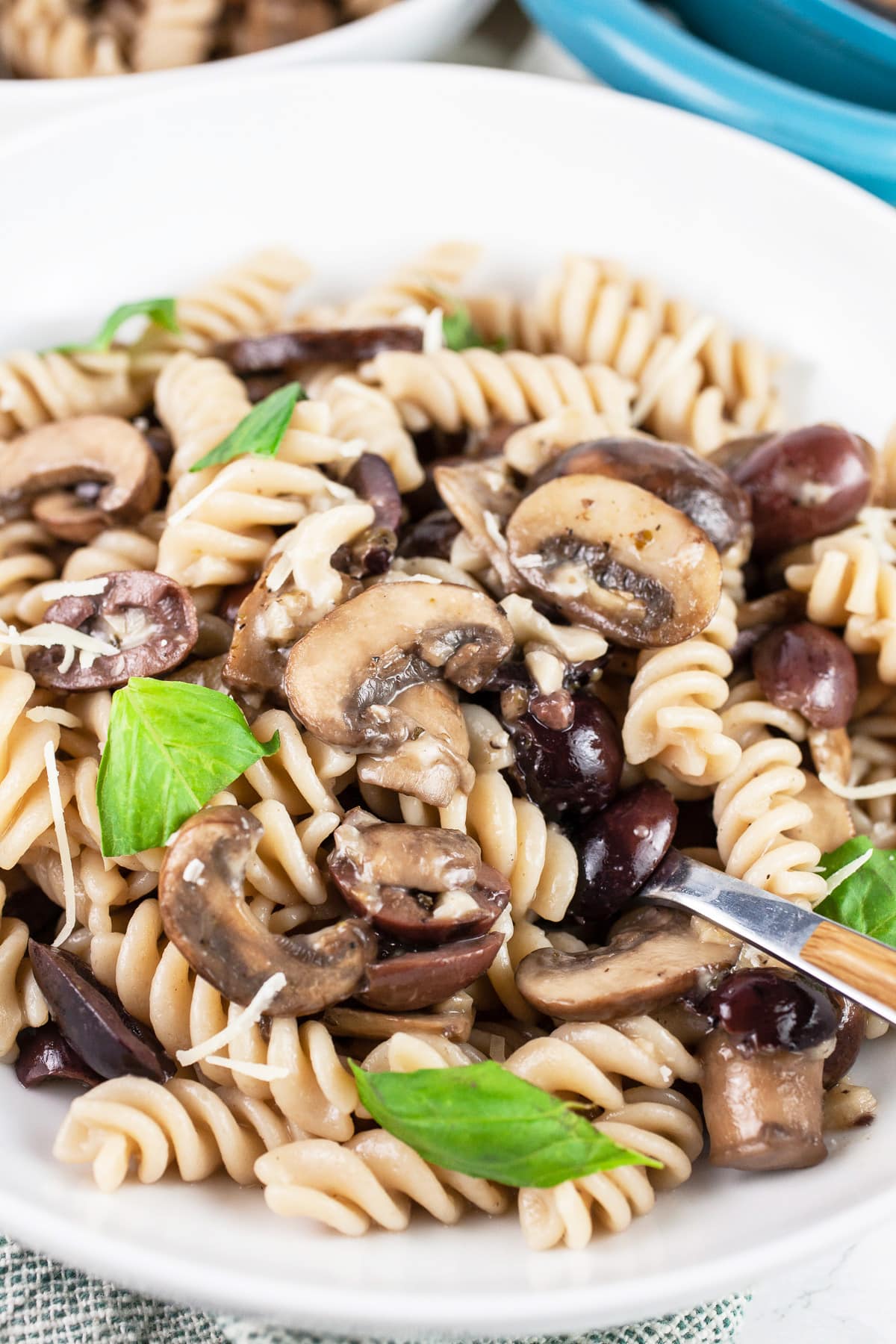 #AD This Mushroom and Olive Pasta recipe makes the perfect easy weeknight dinner! It's made with Barilla Red Lentil Pasta so it's full of plant-based protein and gluten free. This healthy vegetarian pasta has sauteed cremini mushrooms and Kalamata olives. It's tossed in a light and flavorful sauce. A great anytime meal or Valentine's dinner! @BarillaUS #TeamCleanPlate #pasta #mushrooms #olives #vegetarian #glutenfree Mushroom olive pasta in white bowl with fork garnished with fresh basil.