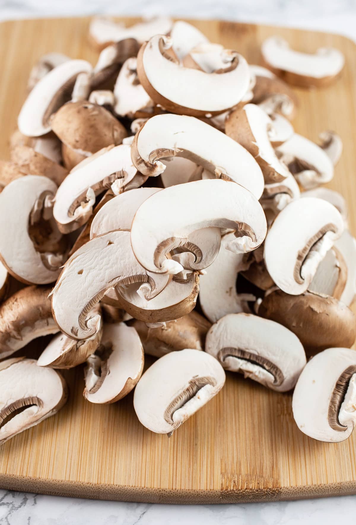 Sliced mushrooms on wooden cutting board.