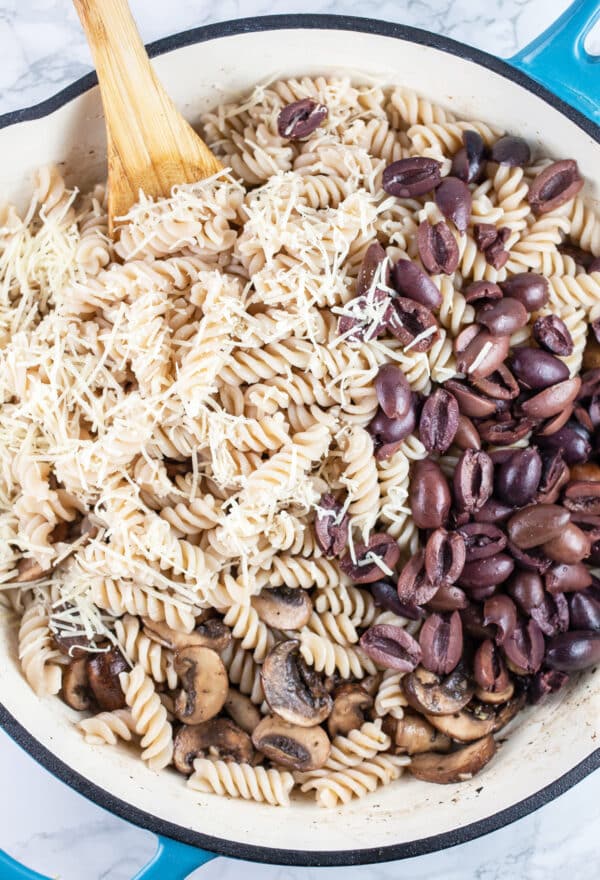 Cooked pasta, mushrooms, Kalamata olives, and grated Parmesan cheese in skillet.
