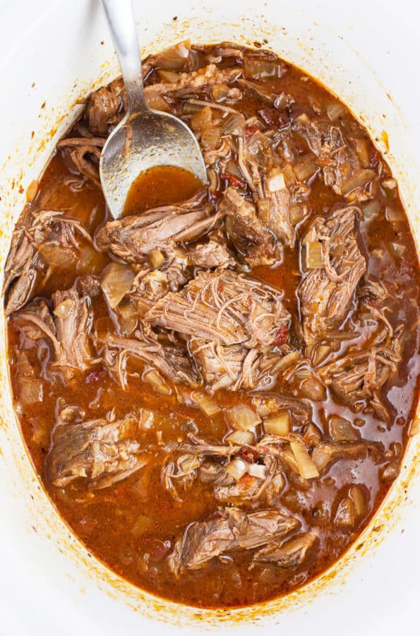 Shredded beef barbacoa in slow cooker with spoon.