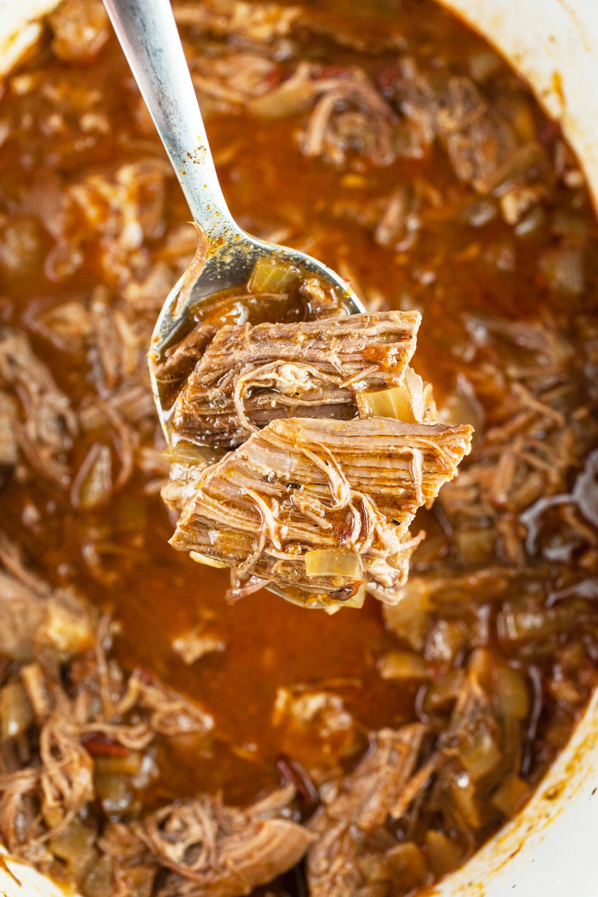 Cooked shredded Mexican beef on spoon lifted from slow cooker.