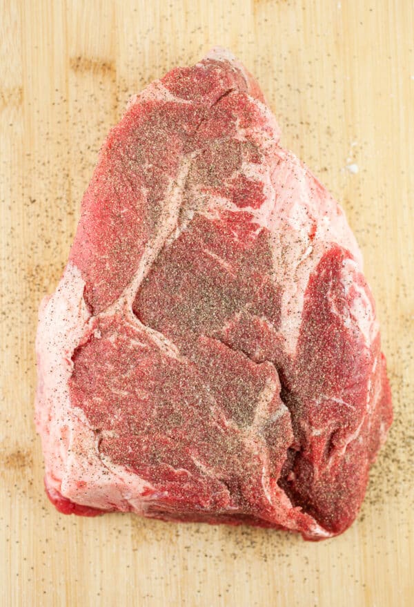 Seasoned raw chuck roast on wooden cutting board.