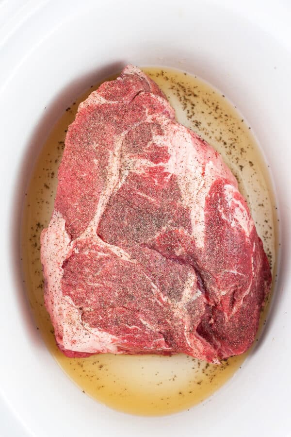Uncooked seasoned beef chuck roast in slow cooker.