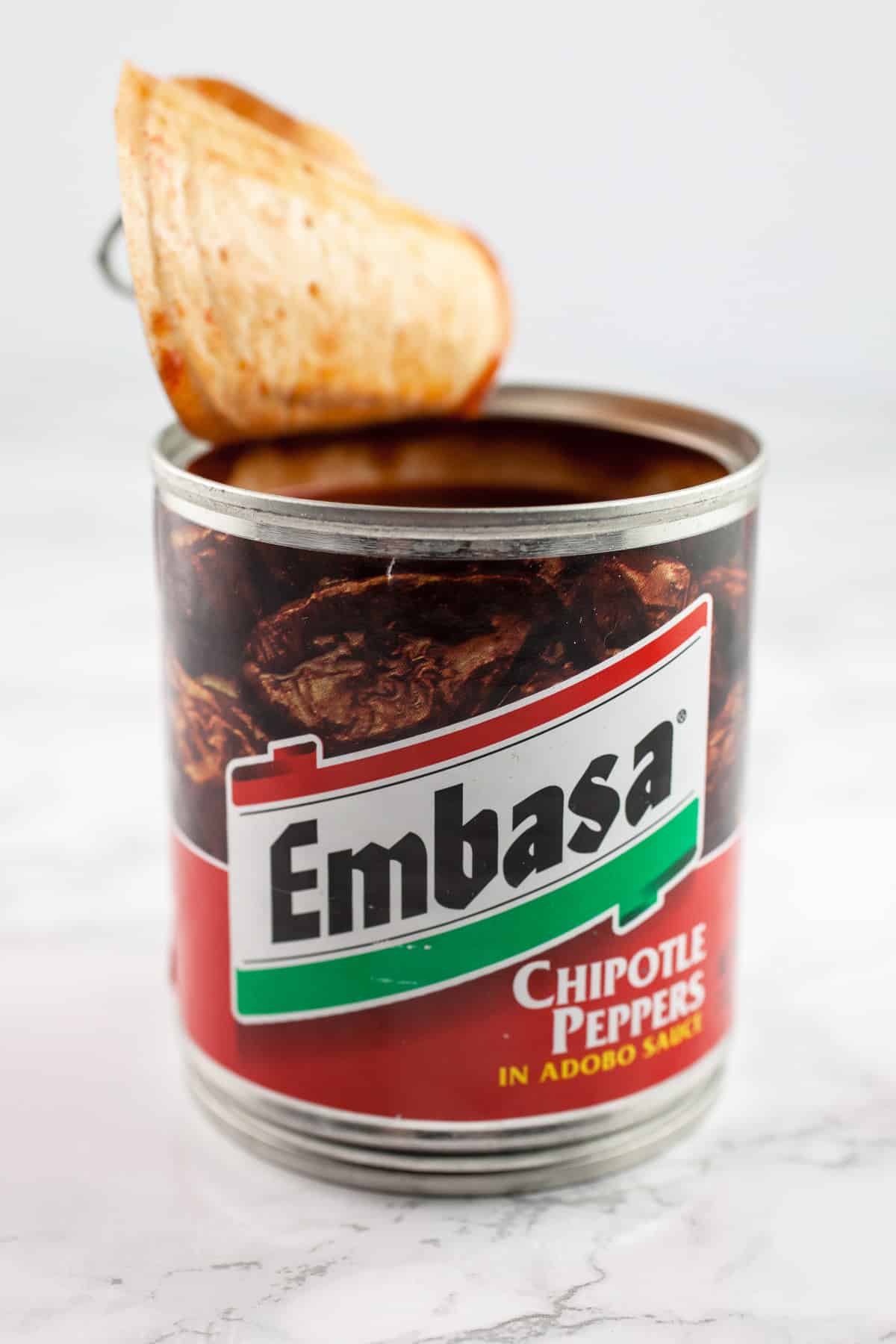 Opened can of chipotle peppers in adobo sauce on white surface.