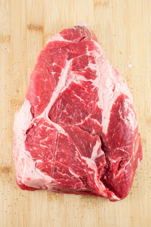 Raw beef chuck roast on wooden cutting board.