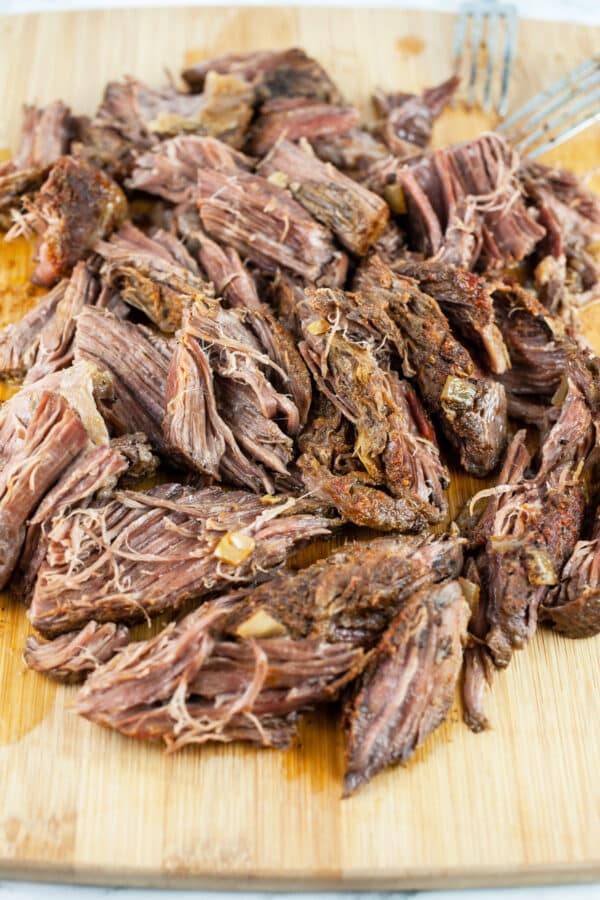 Shredded beef chuck roast on wooden cutting board.