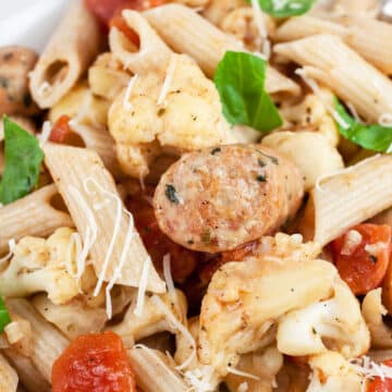 Cauliflower, tomato, and sausage penne pasta in white bowl garnish with fresh basil.