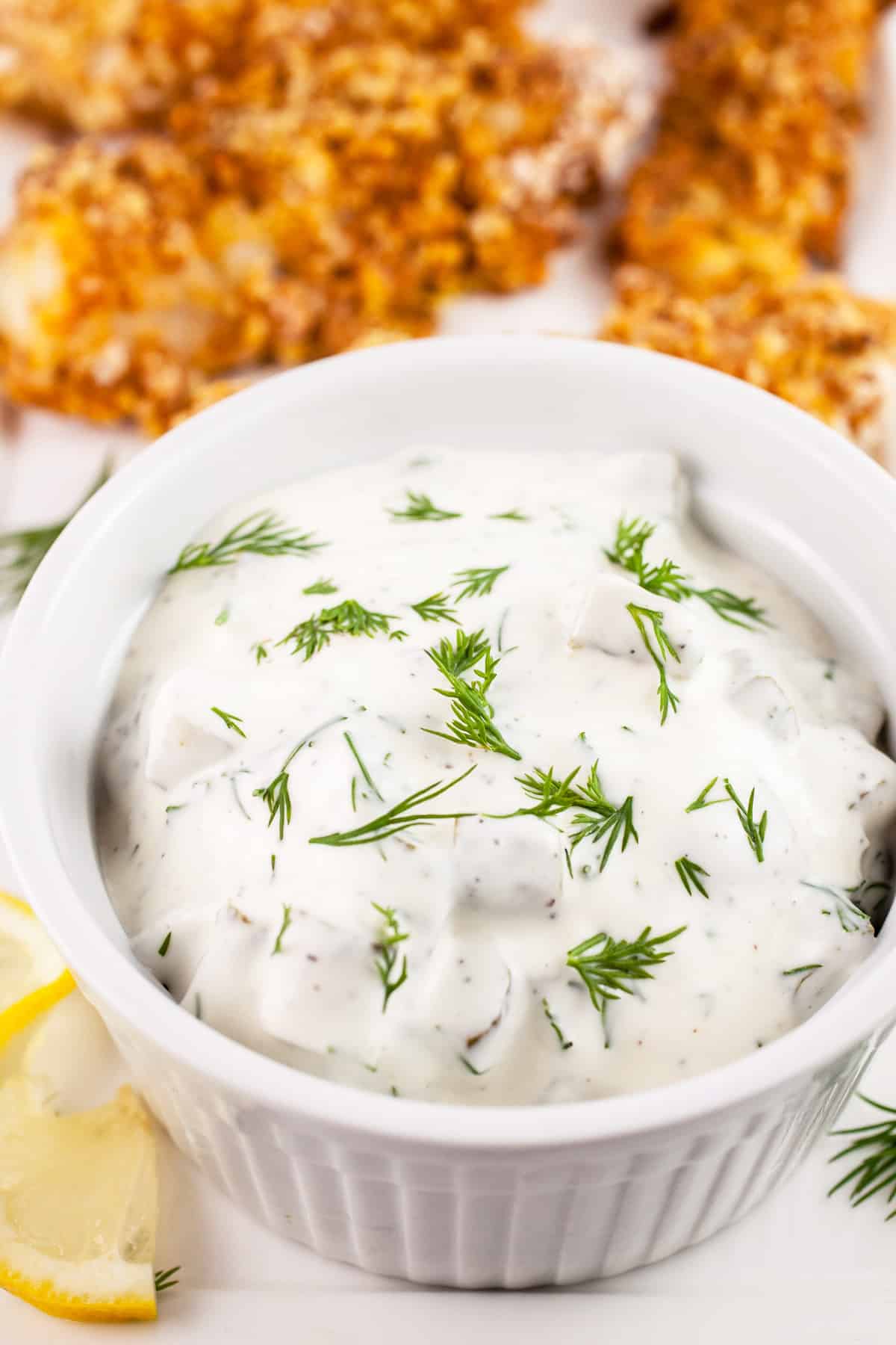 Dill pickle tartar sauce in small white bowl with walleye fingers on platter.