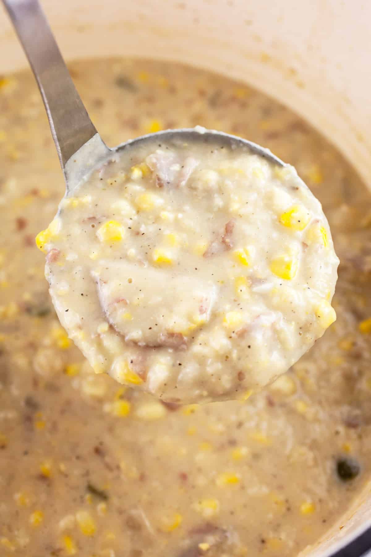 Scoop of potato corn chowder lifted from Dutch oven with metal ladle.