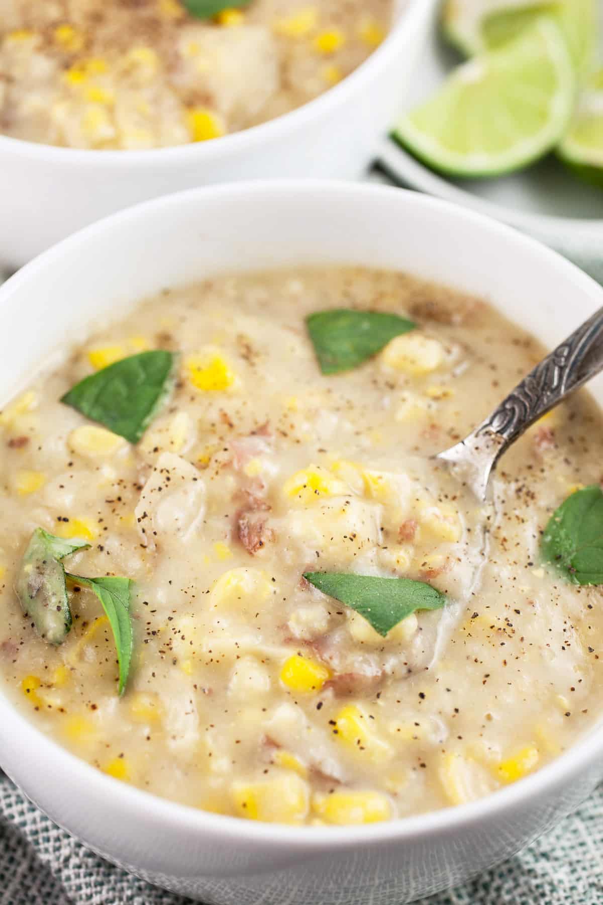 Vegan potato corn chowder garnished with Thai basil with lime wedges in white bowl.
