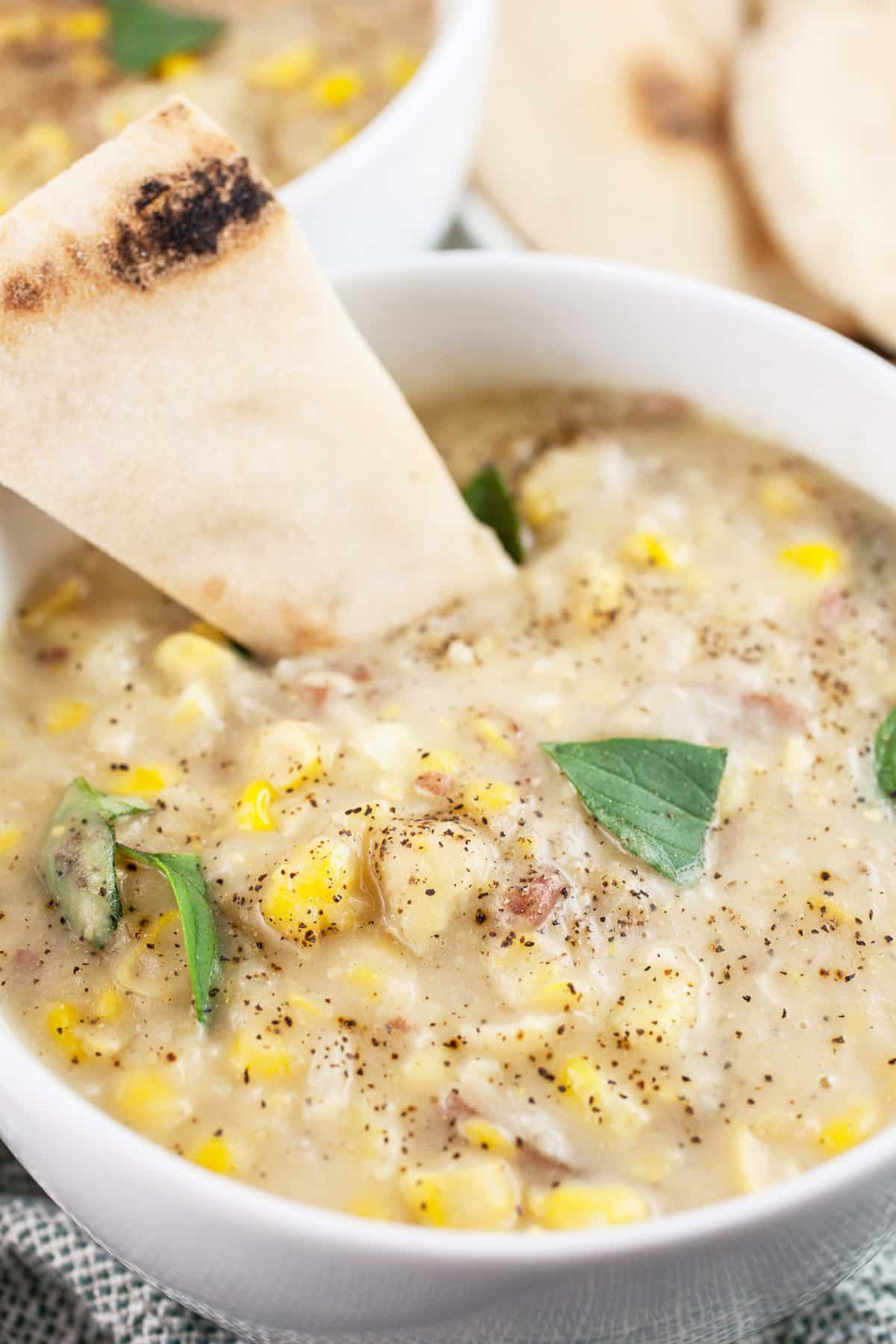 Vegan potato corn chowder with slice of flatbread and Thai basil in white bowls.