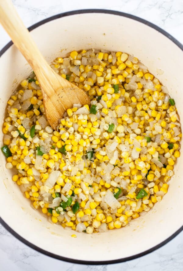 Sautéed garlic, onions, jalapenos, and sweet corn in Dutch oven with wooden spoon. 