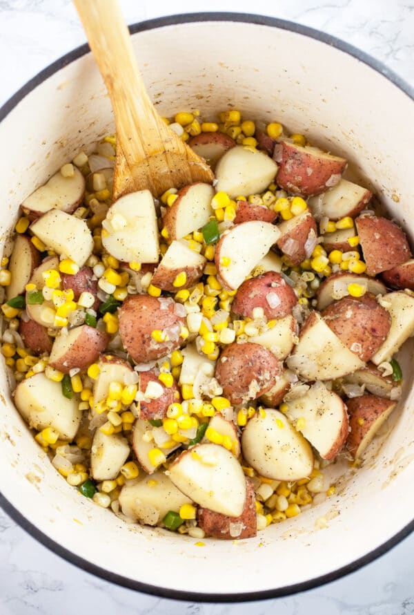 Sweet corn and potatoes sautéed in Dutch oven with wooden spoon.