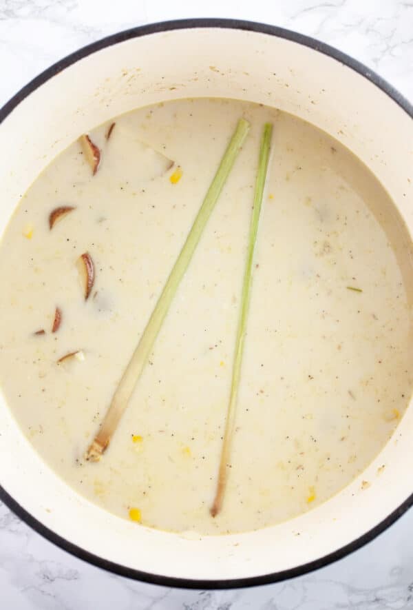 Vegan potato corn chowder broth with lemongrass stalks in Dutch oven.
