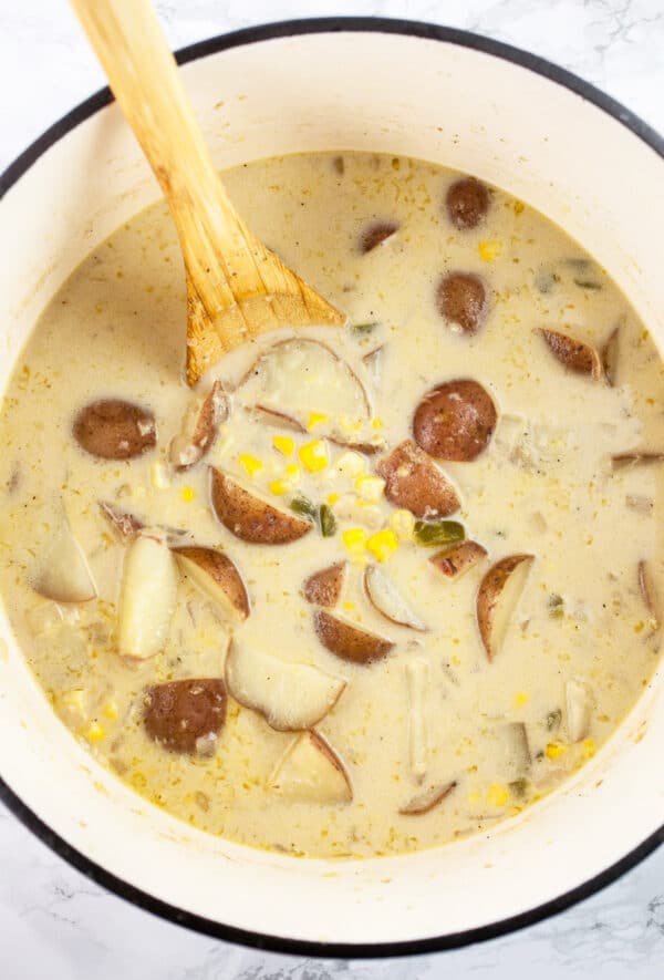 Cooked potato corn chowder in Dutch oven with wooden spoon.