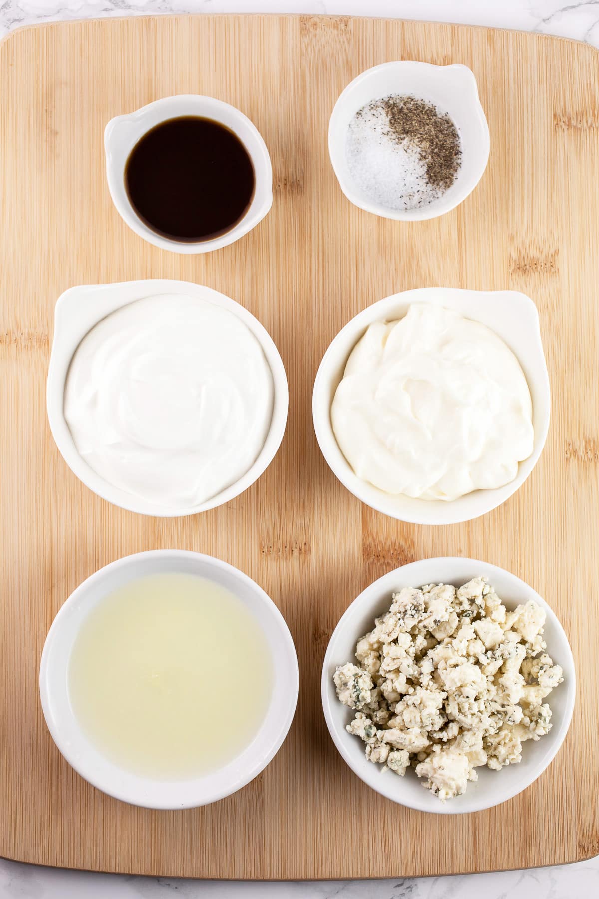Blue cheese crumbles, lemon juice, mayo, sour cream, Worcestershire sauce, and salt and pepper in small white bowls on wooden cutting board.